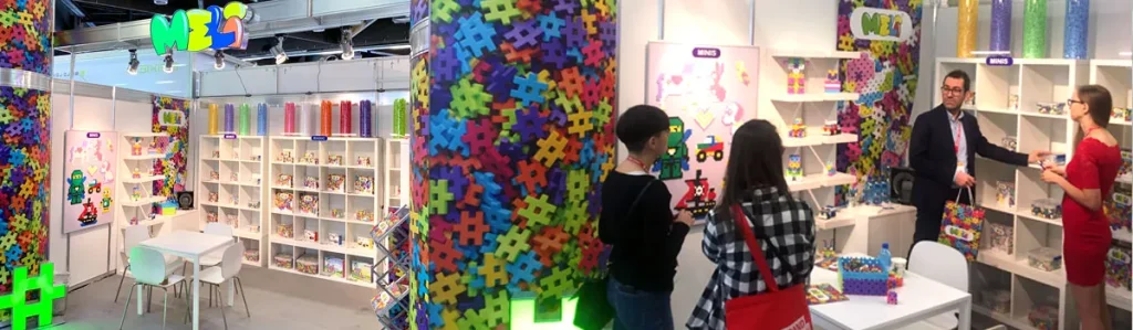 Stand de MELI en feria de juguetes con expositores llenos de sets de construcción y visitantes observando los productos
